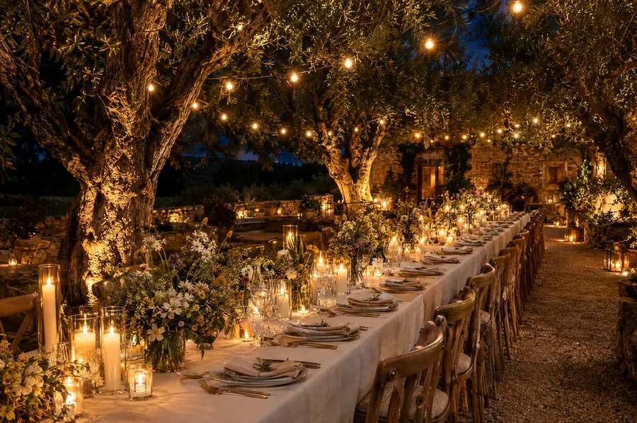 Long candlelit table under olive trees